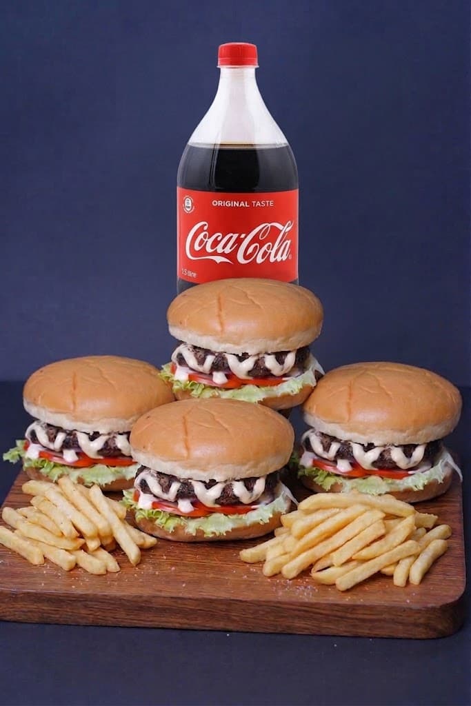 Four burgers on a wooden board with fries and a 1.5 litre bottle of Coca-Cola