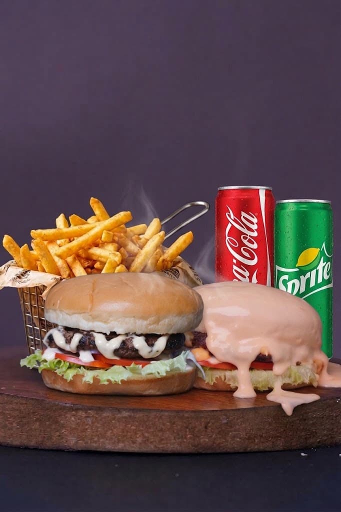 Two burgers with a basket of fries, a Coke can and a Sprite can