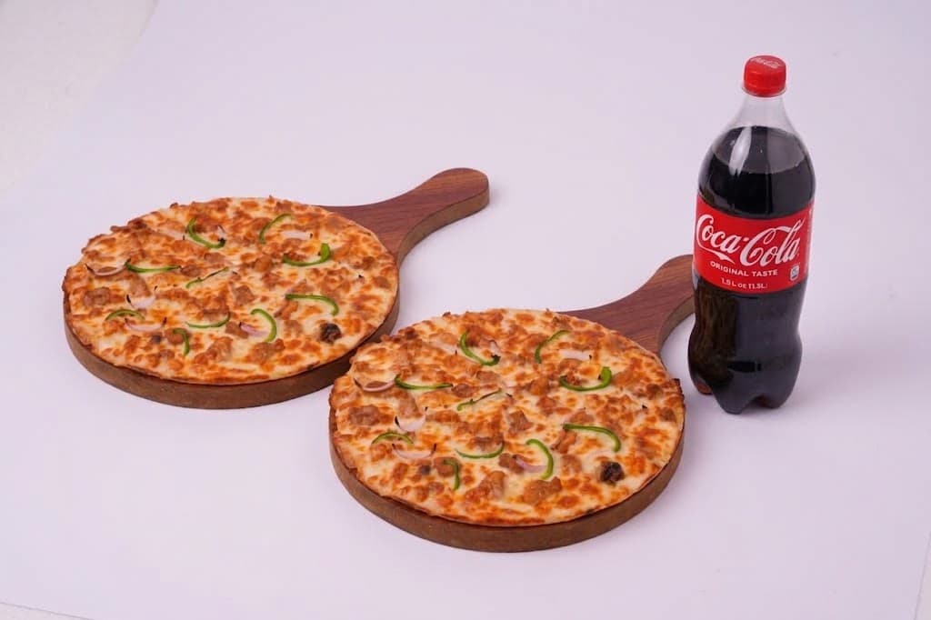 Two large pizzas on a table with a 1.5 litre drink bottle