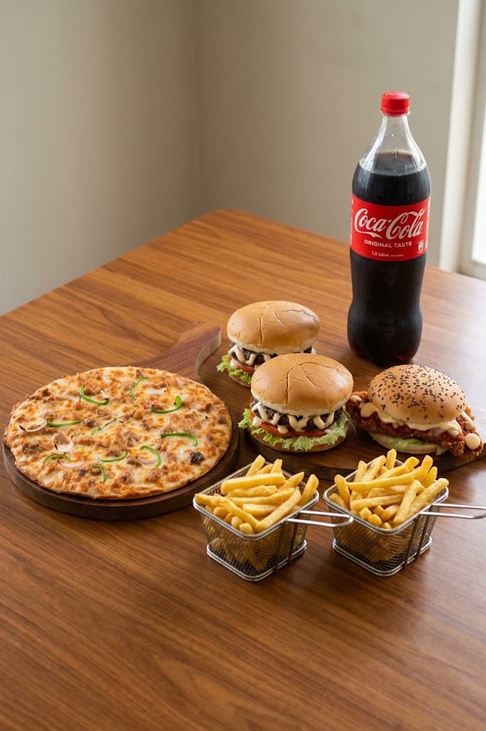 A pizza, three burgers and two baskets of fries on a wooden table with a 1.5 litre Coca-Cola bottle