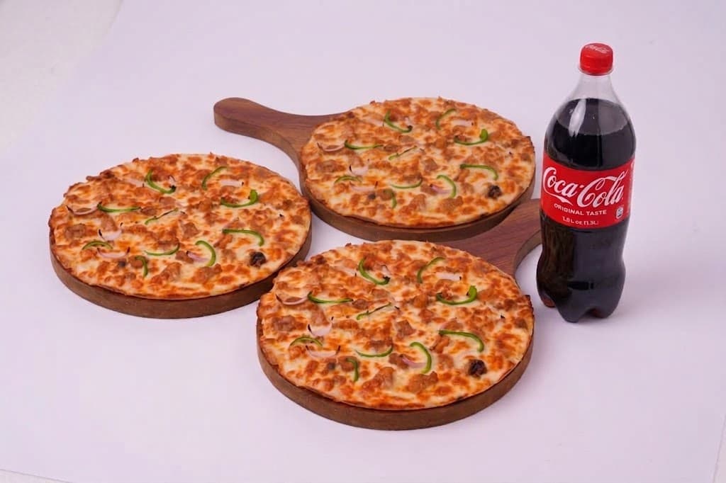 Three large pizzas on a table with a 1.5 litre drink bottle
