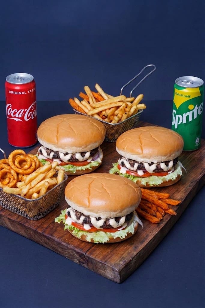 Three burgers on a wooden board with fries, a Coke can and a Sprite can